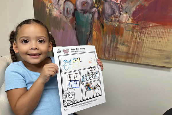 A child holds up her finished Super Day Replay printable showing her experience painting.