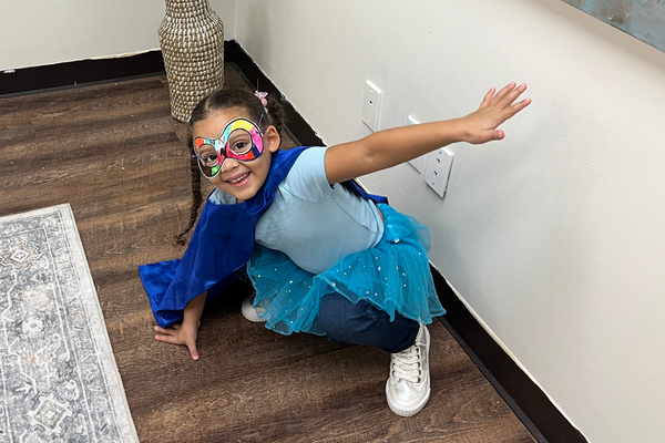 A child is ready to go on a Super Reader adventure wearing a superhero costume including a cape and her Super Reader mask.