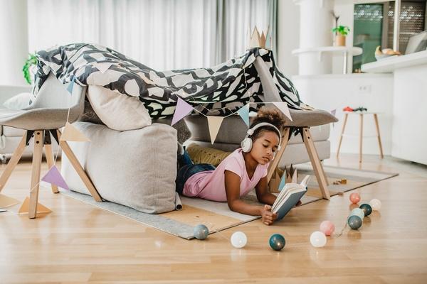 Child having quiet time in a homemade fort. The child is wearing headphones and reading a book.
