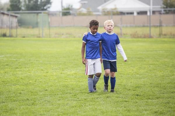 Two children walk across a field wearing sports uniforms.
