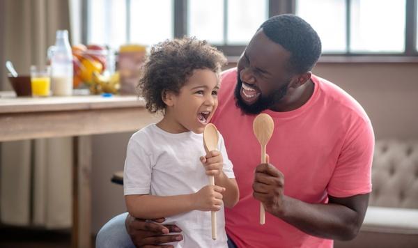 Father and daughter singing together into wooden spoons.