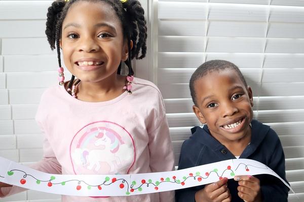 Two kids holding up thumbprint holiday lights activity.