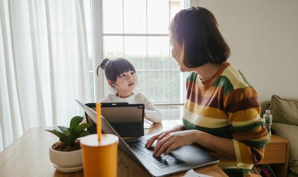 Una mamá y su hijos sentados en la mesa con una laptop y una tableta.
