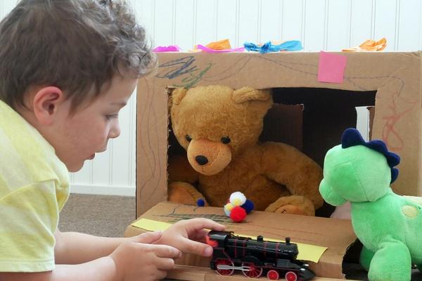 Child sitting at a decorated box with stuffed animals peeking through a window.