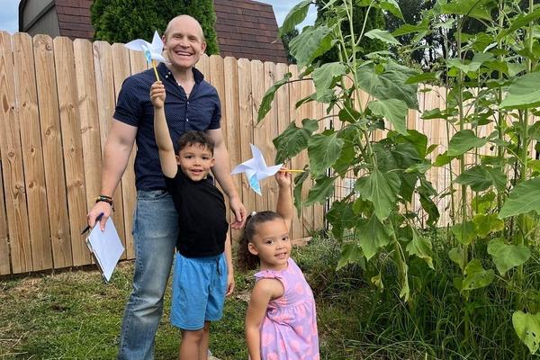 Dad and two kids hold up their finished pinwheels in their backyard.