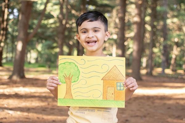 Un niño sostiene un dibujo que muestra las diferentes formas en que el viento puede moverse entre un árbol y una casa.