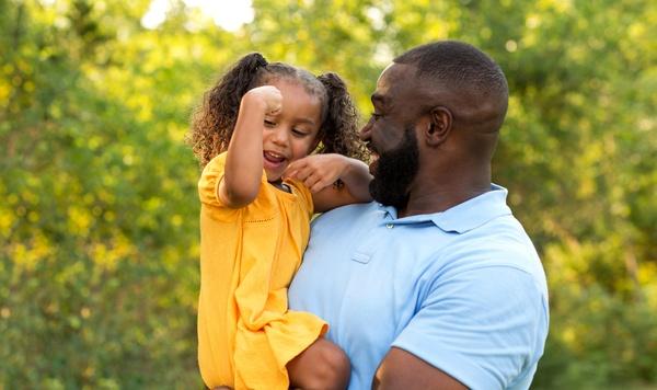 Father holding daughter while she shows off her arm muscles.