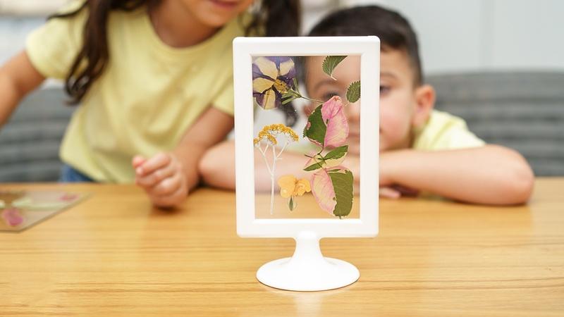 Two children looking at their framed artwork of pressed flowers.