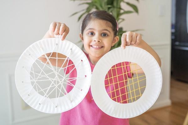 A child holding two finished spider web test plates.
