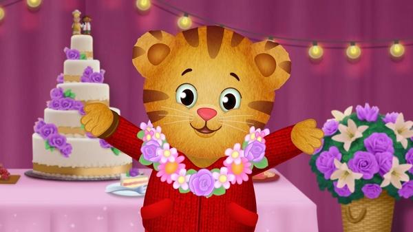 Daniel Tiger wearing a lei and standing in front of a wedding cake.