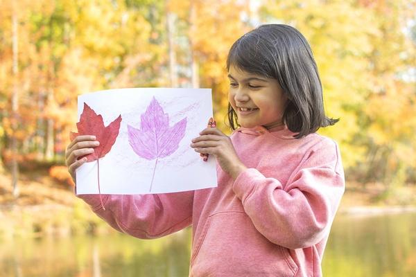 A child admires their fall leaf art.