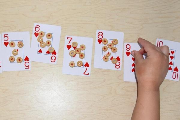 A child places circle shaped cereal pieces on playing cards to match the number on the card.