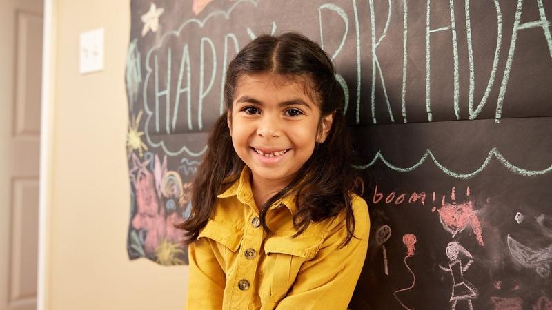 Child standing in front of birthday party banner.