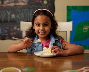 Girl smiling as she has a plate of cake in front of her.