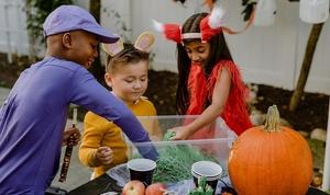 More children in costumes reaching into the swamp monster sensory bin.