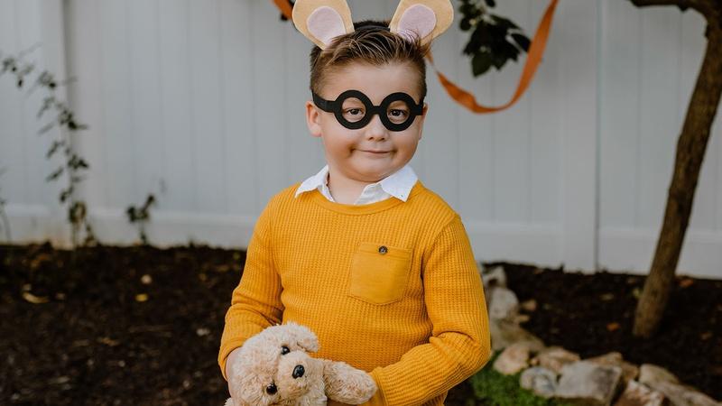 Child dressed up as Arthur and holding a stuffed animal dog to represent Arthur's dog Pal.
