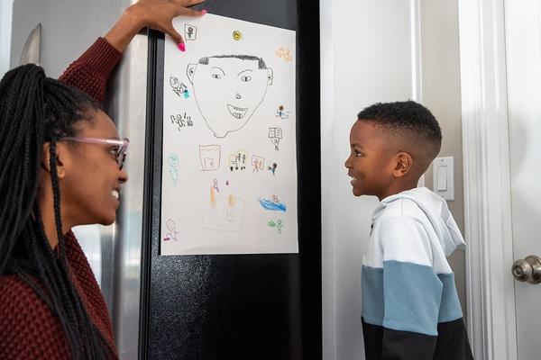 A child looks at their self-portrait with a parent beside them.