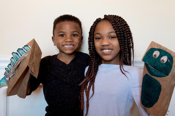 Two children holding their completed stegosaurus puppets.