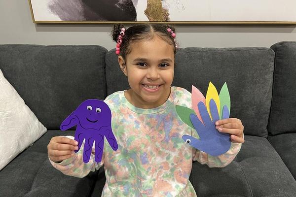 Una niña luce sus manualidades de una medusa y un pájaro hechos con la huella de su mano.