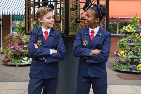 Two Odd Squad Agents are smiling while standing in front of a flower shop.