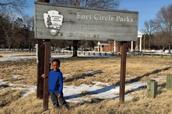 A child stands with a sign that shows the name of a national park.