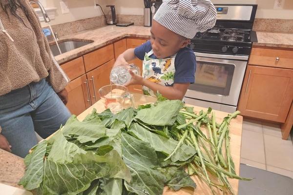 Child has finished stemming the collard greens and is pouring vinegar into a measuring cup to prepare to wash the greens.