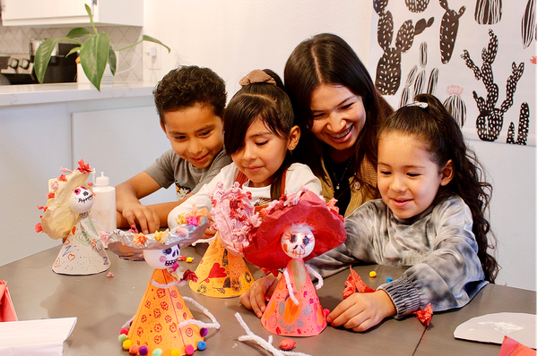Image of a grownup with three children with their finished Catrina dolls.