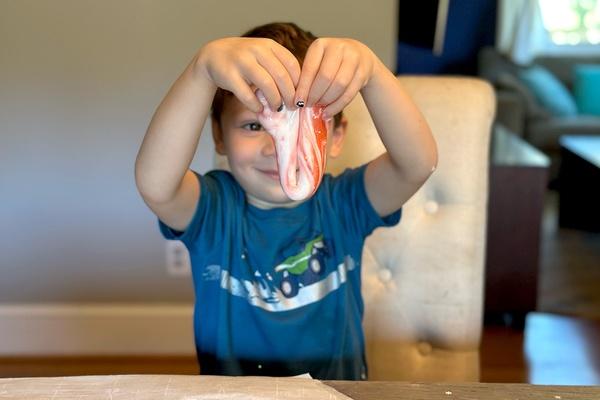 Un niño sonriente sostiene su slime rojo y blanco encima de la mesa.