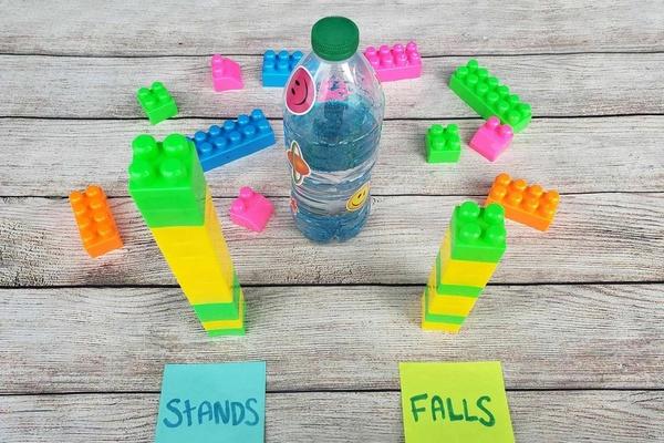 A water bottle with sparkly blue water stands alongside two towers of colorful plastic blocks representing the number of "stands" and "falls" in this fun bottle-flipping game.