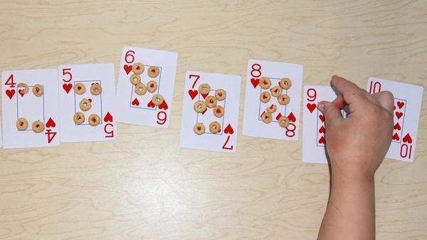 A child places circle shaped cereal pieces on playing cards to match the number on the card.