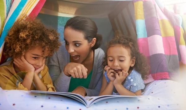 A parent reads to two kids in a homemade fort.