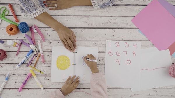 A child draws pictures in a homemade counting book.