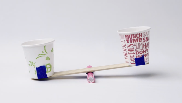 Two paper cups are taped on a ruler to make a homemade scale.