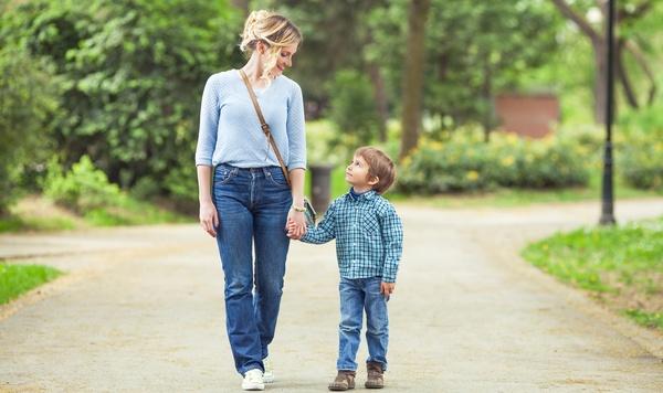 Mother and son holding hands while walking in a park together.