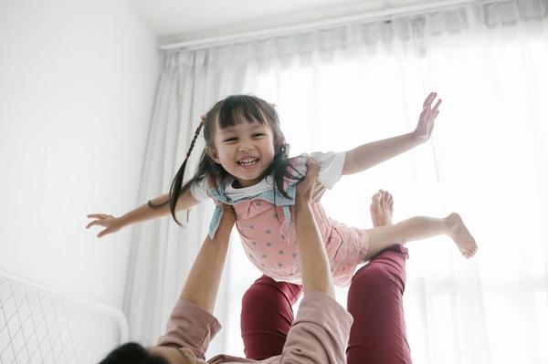 A parent holds a child up in the air so that the child can pretend to be flying.