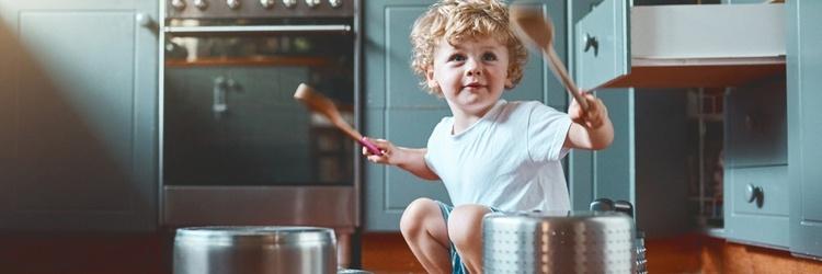 A child bangs on pots and pans with a wooden spoon.