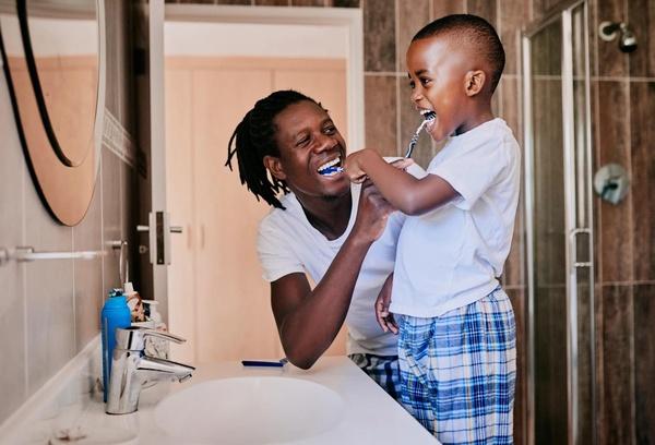 A father and child brush their teeth together.