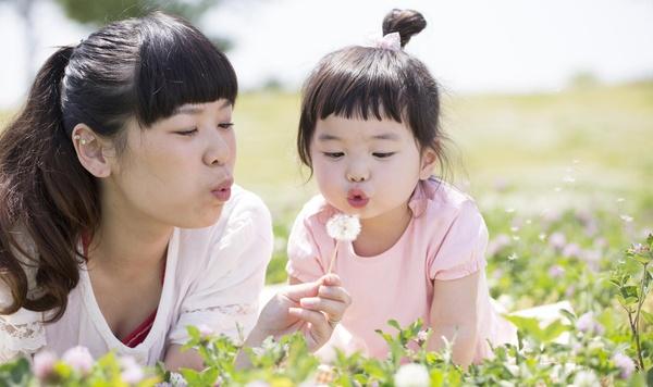 Image of mother and daughter blowing on a dandelion.