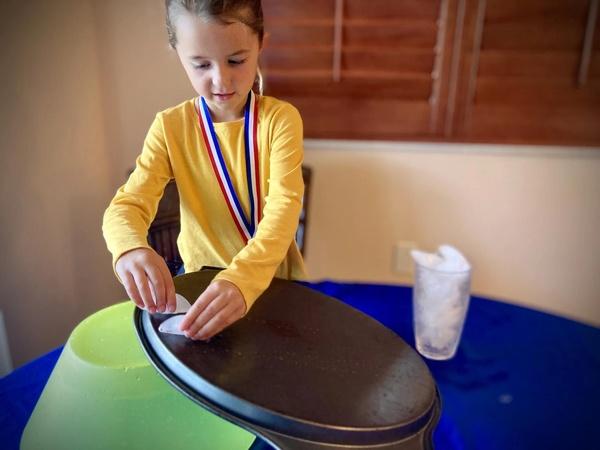 A child slides ice cubes along the bottom of a serving tray.
