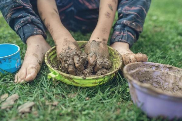 A child plays with mud in a bowl while sitting on grass.