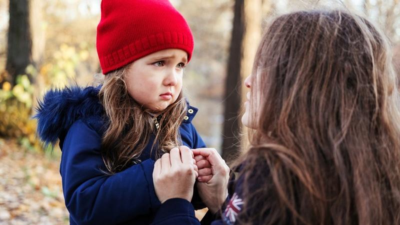 Young girl looks worried while mother holds her hands.
