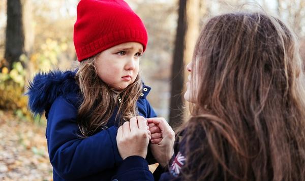 Young girl looks worried while mother holds her hands.