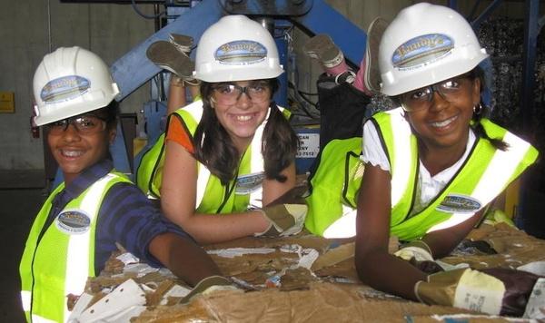Tres niñas con chalecos de seguridad para la construcción y cascos clasificando la basura.